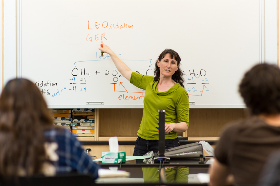 Dr. Heather Price lectures at whiteboard in front of a chemistry students.