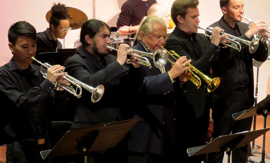 Fred Radke and ensemble play trumpets on stage.