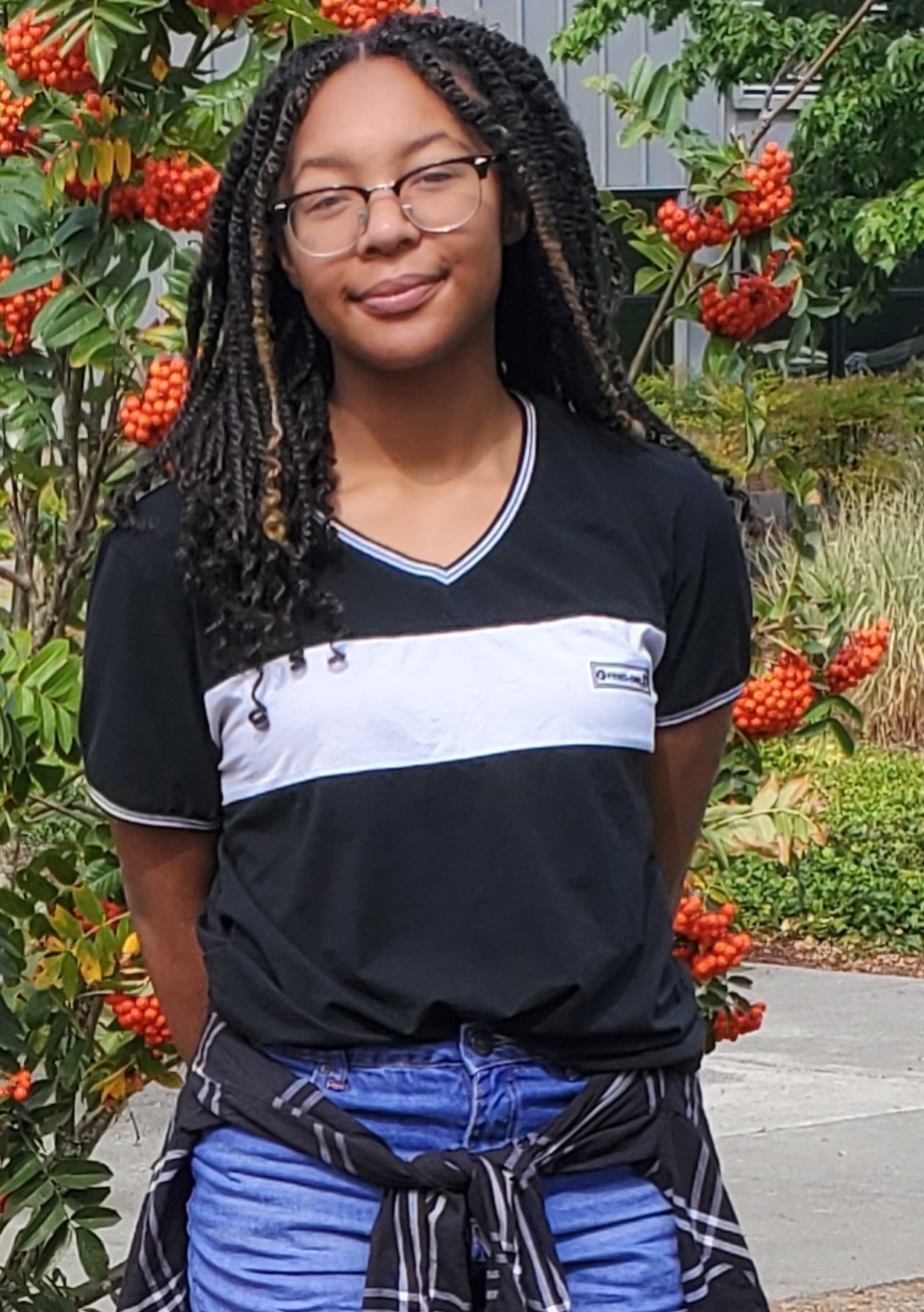 female student standing next to green bush