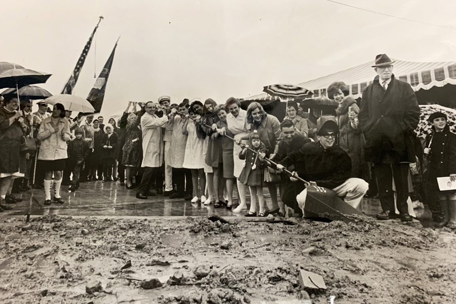 Black and white photo of NSC groundbreaking; a long shovel digs in the muddy ground. 