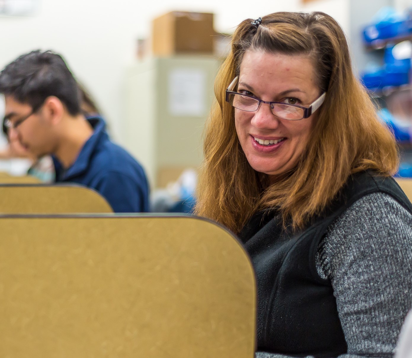 female sitting at desk with glasses smiling