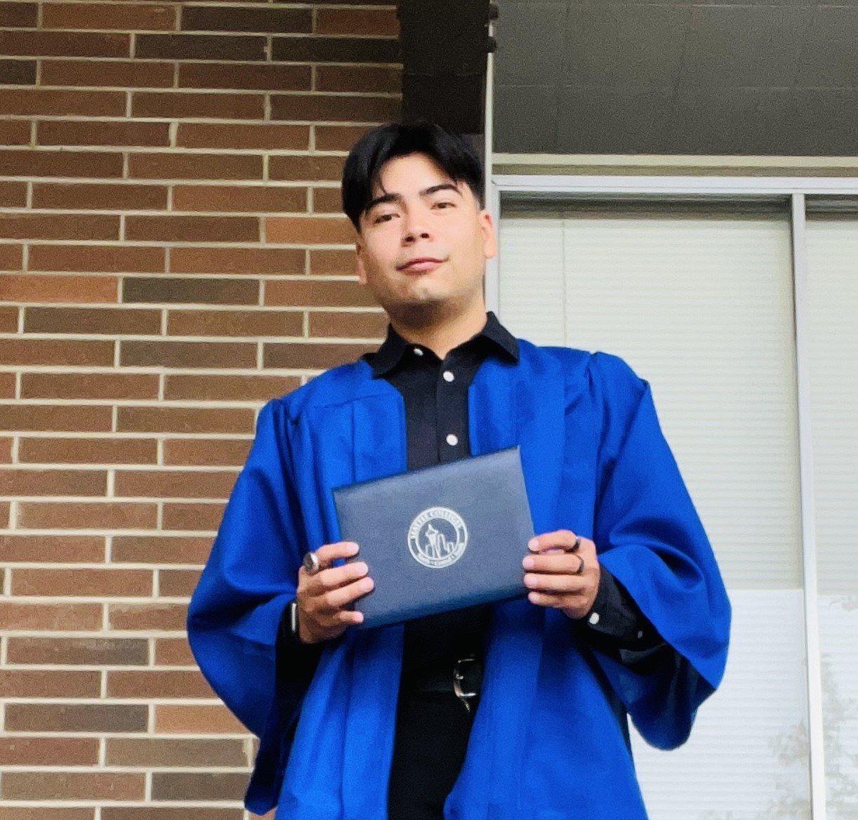 male wearing a blue graduation gown holding a diploma 