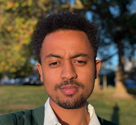male wearing a green sweater with a white collar with trees in background 