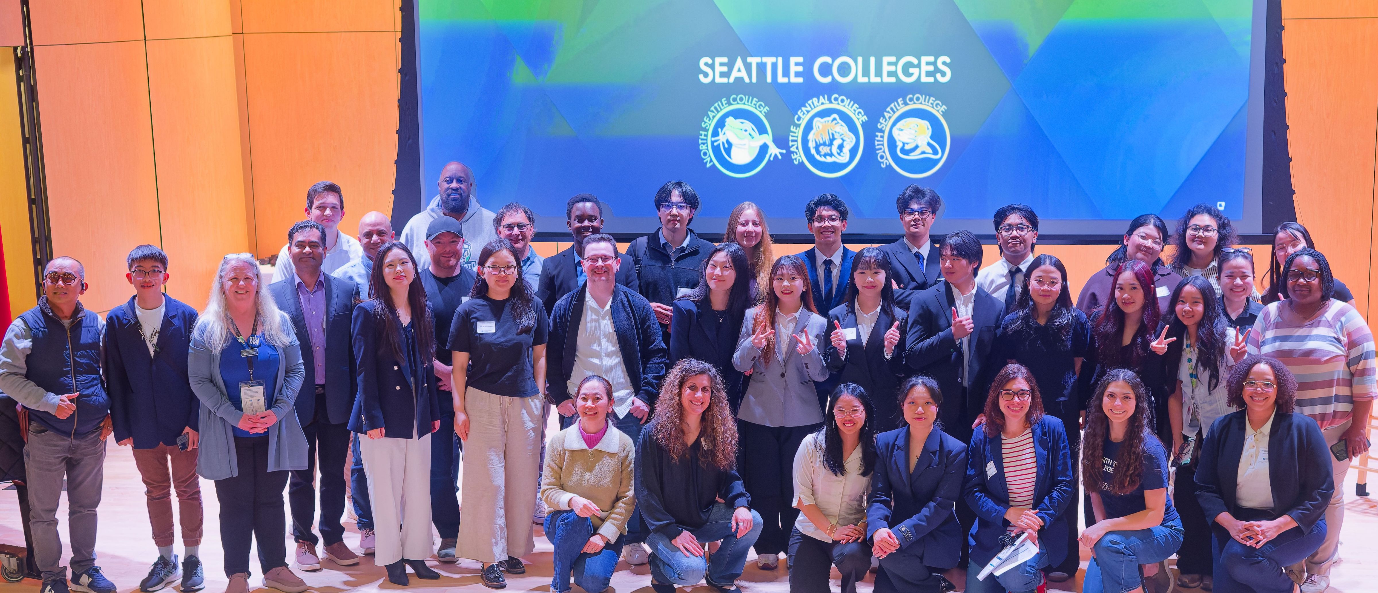 large group of students standing on a stage with blue background on a screen with Seattle Colleges on it 
