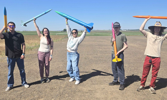students holding up rockets standing outside in desert land