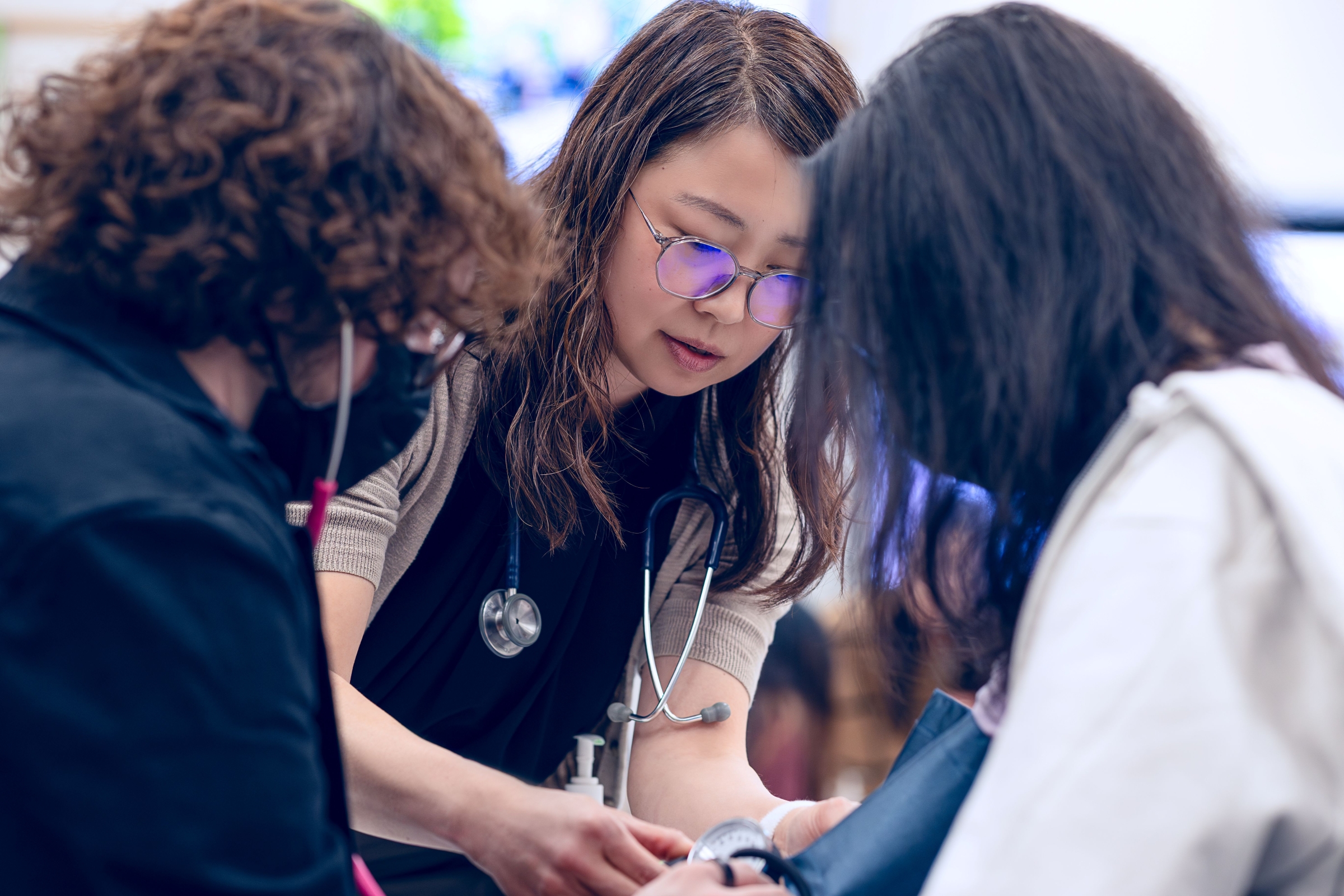 a female wearing glasses and a male wearing stethoscopes putting a blood pressure cuff on someone 
